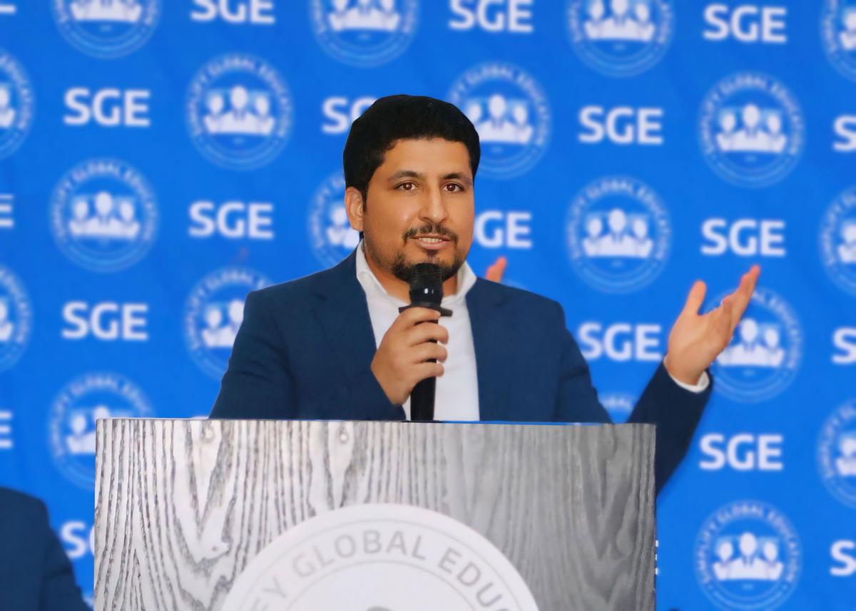 SGE speaker presenting at podium with blue backdrop