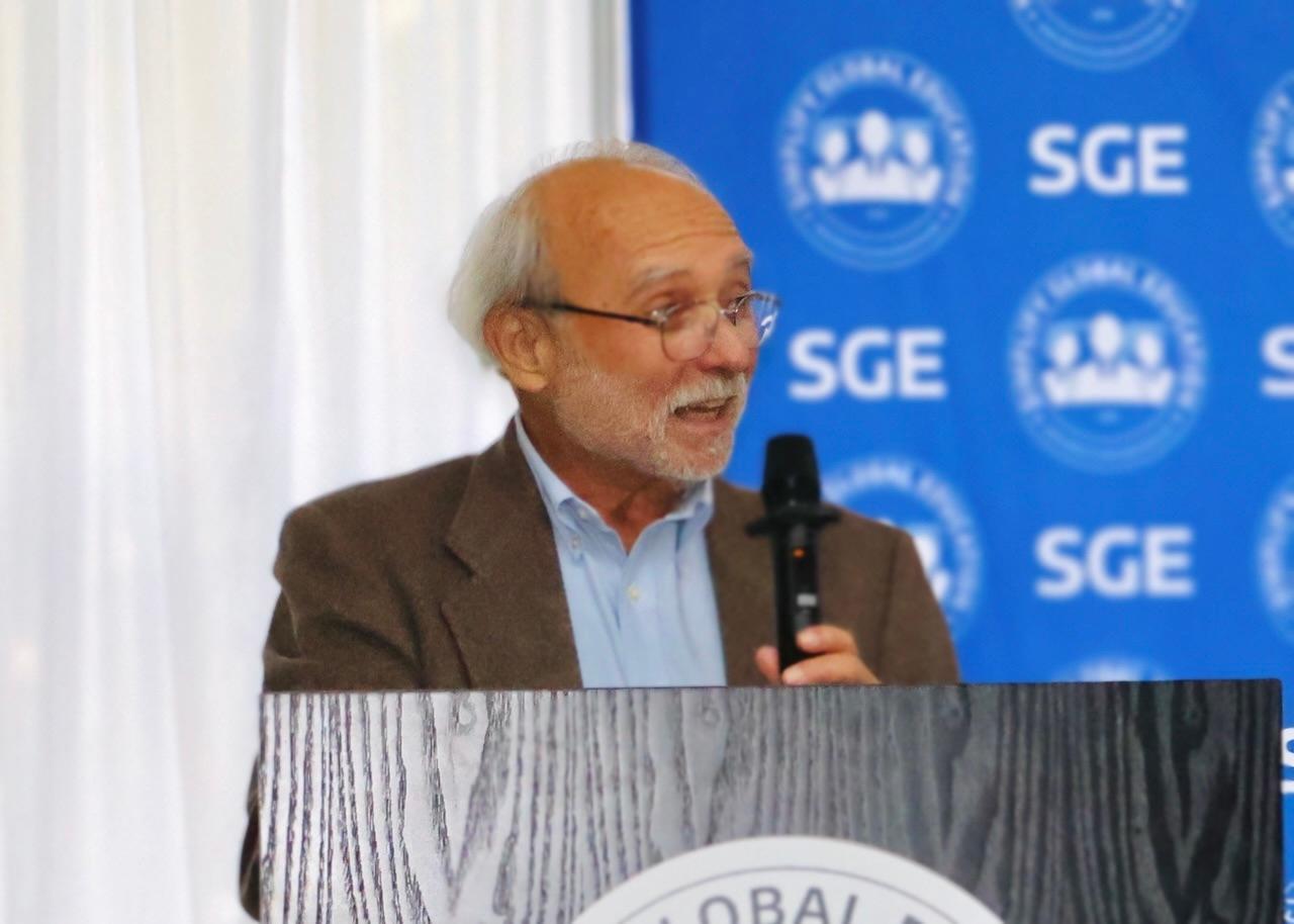 SGE speaker presenting at podium with blue backdrop